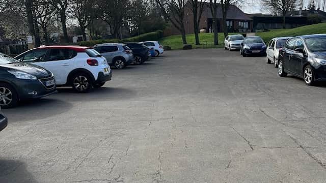 Free parking area in Wakefield, Yorkshire, with several parked cars and trees under a partly cloudy sky.