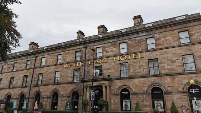 Historic stone building with large windows, "WHITE HART HOTEL" sign, and decorative plants in front.