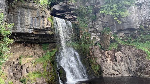 A picturesque waterfall cascading over rocky cliffs into a tranquil pool, surrounded by lush greenery.