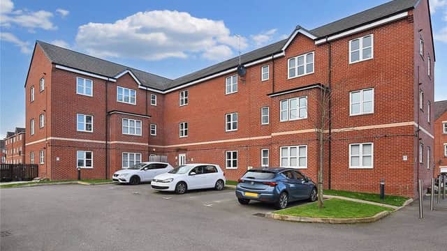 Residential car park featuring multiple parked cars and modern brick buildings under a blue sky in Tingley, Yorkshire.