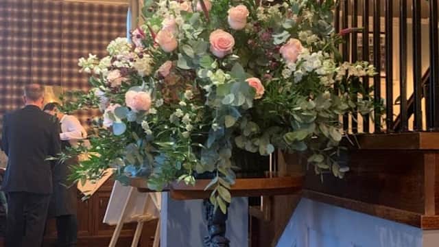 Elegant floral arrangement featuring pink roses and greenery, displayed on a decorative stand in a stylish interior.