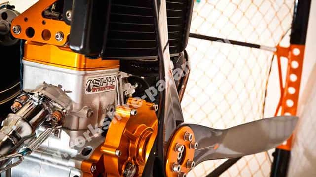 Close-up of a paramotor engine with orange and silver components, showcasing intricate mechanical details and a propeller.
