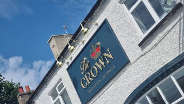 The Crown pub sign with gold lettering, blue background, and a crown logo, set against a clear blue sky.