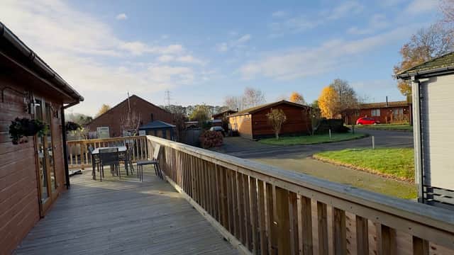 Wooden deck with outdoor seating, surrounded by lodges and trees under a clear blue sky in Wilberfoss, Yorkshire.