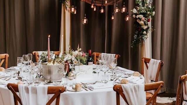 Elegant round dining table set for a wedding, adorned with white linens, floral arrangements, candles, and hanging lights.