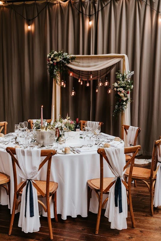 Elegant round dining table set for a wedding, adorned with white linens, floral arrangements, candles, and hanging lights.