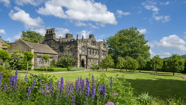 Historic East Riddlesden Hall features stone architecture, lush gardens, and a bright blue sky.
