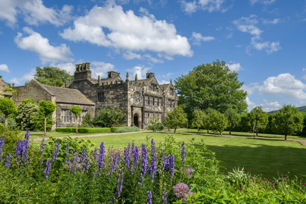 Historic East Riddlesden Hall features stone architecture, lush gardens, and a bright blue sky.