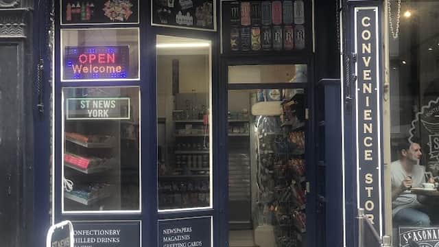 ST NEWS York storefront with open sign, displaying convenience items, snacks, and drinks. Brick building with blue facade.