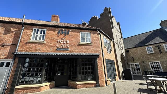 Red brick building with large windows, sign reading "Four Cats" and outdoor seating area under a clear blue sky.