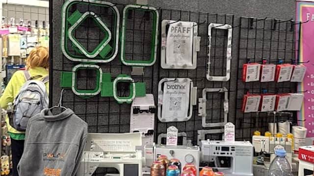 BAi Embroidery Machine display with colorful threads, embroidery hoops, and a grey hoodie on a stand at a trade show.