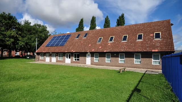 Community center with a sloped roof, solar panels, and green lawn, surrounded by trees and a blue fence.