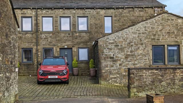 Stone cottages with a red car parked in front, surrounded by greenery and a cobblestone driveway.