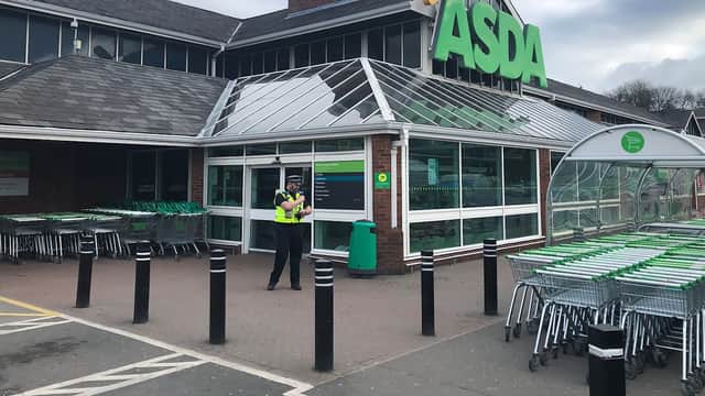 ASDA Pharmacy storefront with shopping carts outside and a security guard standing at the entrance.
