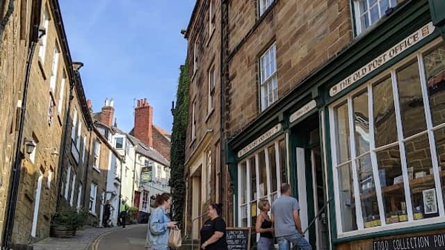 Busy street scene on Thorpe Lane, featuring charming stone buildings, a café, and people chatting outside.