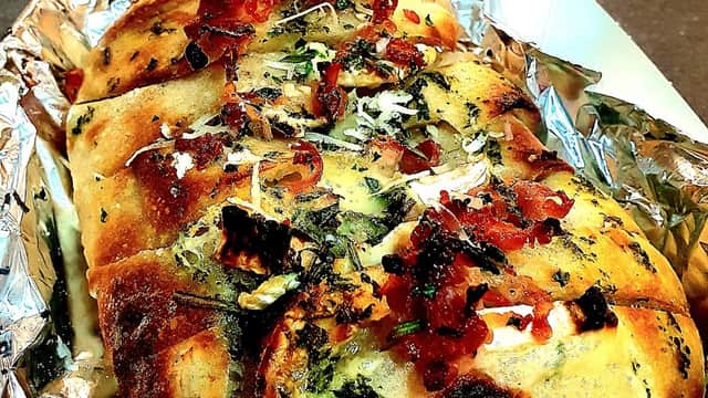 Golden, crusty bread topped with herbs, cheese, and crispy bits, served in a foil tray at New Yorkshire Food Co.
