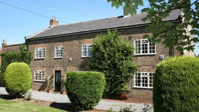 Charming brick manor house surrounded by neatly trimmed hedges and a gravel pathway under a clear blue sky.
