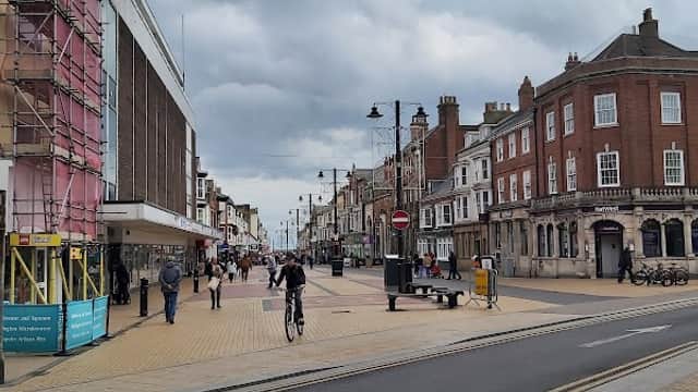 Pedestrian street with shops, cyclists, and cloudy skies in Barmston, Yorkshire.