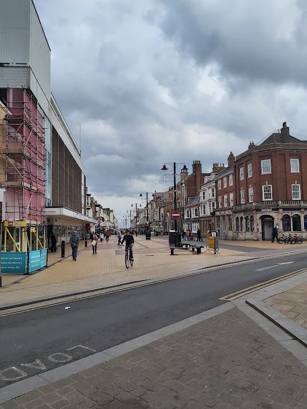 Pedestrian street with shops, cyclists, and cloudy skies in Barmston, Yorkshire.