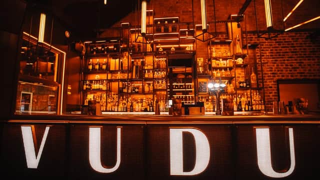 Illuminated bar with "VUDU" signage, shelves lined with bottles, and warm lighting in a stylish pub setting.