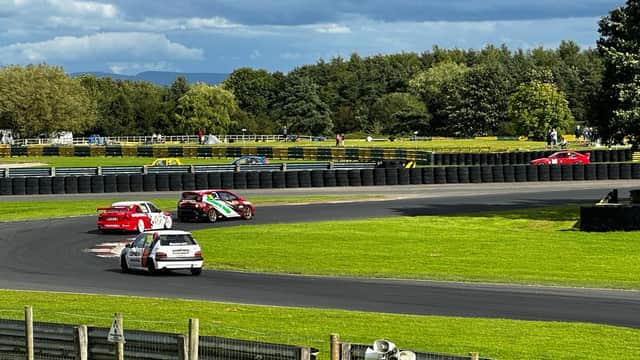 Cars racing on a track at Croft Circuit, surrounded by green trees and a cloudy sky.