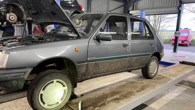 A grey car on a lift in a garage, with tools and other vehicles visible in the background.