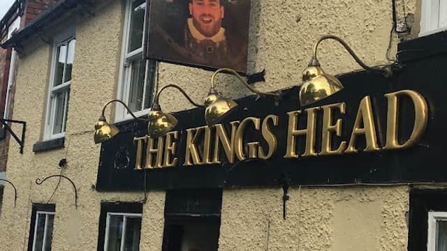 The Kings Head pub features a sign with a man's portrait and golden lettering, surrounded by outdoor lighting.