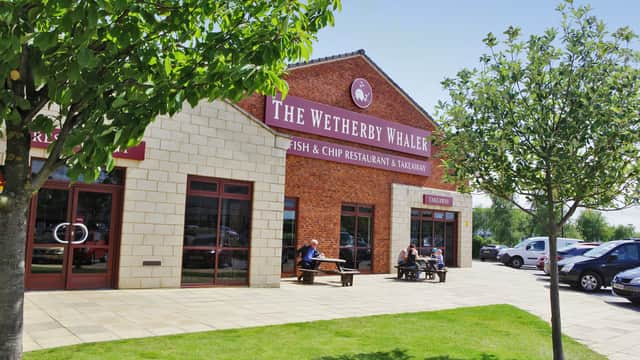 Red-brick fish and chip restaurant with outdoor seating, surrounded by green lawn and trees under a clear blue sky.