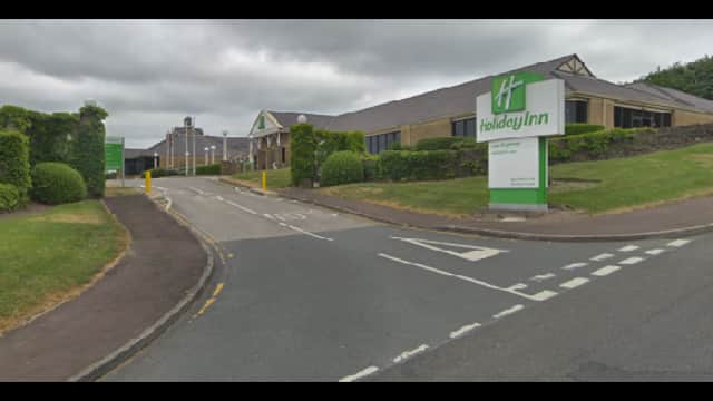 Entrance to Holiday Inn with green signage, surrounded by neatly trimmed hedges and a cloudy sky in Brighouse, Yorkshire.
