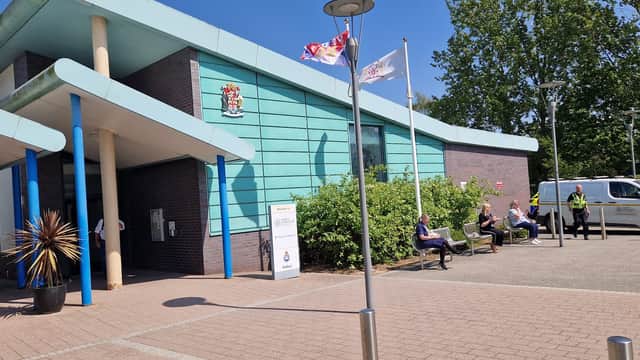 Modern building with teal panels, flags, and people sitting on benches outside the North Yorkshire Council Selby Offices.