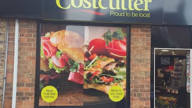Costcutter storefront featuring fresh sandwiches and salads, with a brick wall background and colorful signage.