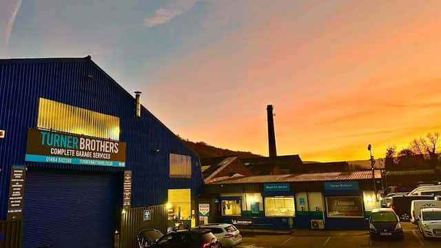 Turner Brothers car parts building at sunset, with parked cars and a chimney in the background.