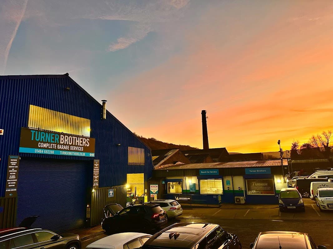 Turner Brothers car parts building at sunset, with parked cars and a chimney in the background.