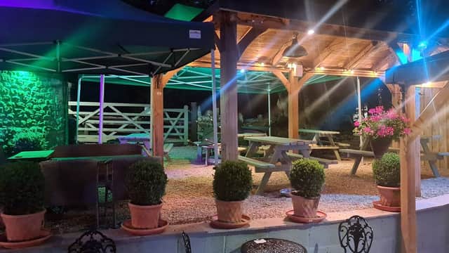 Outdoor dining area at The Blacksmiths Arms, featuring wooden tables, green canopies, and illuminated plants at night.