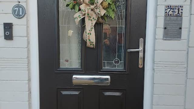 A decorated front door with a wreath featuring greenery and a bow, flanked by two hanging plants.