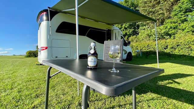 A caravan under a green awning with a table set for drinks, surrounded by lush grass and trees in Fadmoor, Yorkshire.