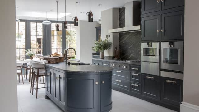 Modern kitchen with dark cabinetry, marble accents, and an island, featuring pendant lights and large windows.