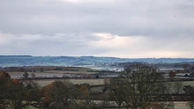 Welburn Village Hall surrounded by rolling hills and trees under a cloudy sky in the Yorkshire countryside.