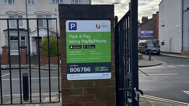 Pay & Display sign for Dartmouth TU car park, with instructions and contact details visible. Cloudy sky in the background.