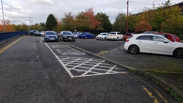 Cars parked in a spacious lot surrounded by trees with autumn foliage under a cloudy sky.