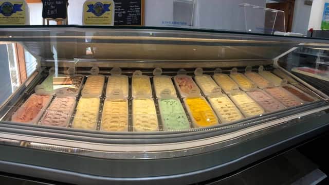 Colorful ice cream tubs displayed in a glass case at Wensleydale Ice Cream Parlour, with a menu board in the background.