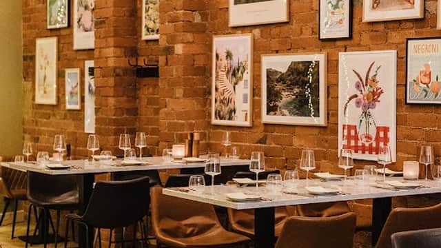 Warm brick walls adorned with colorful artwork, elegant tables set with glasses, and soft lighting create a cozy ambiance.