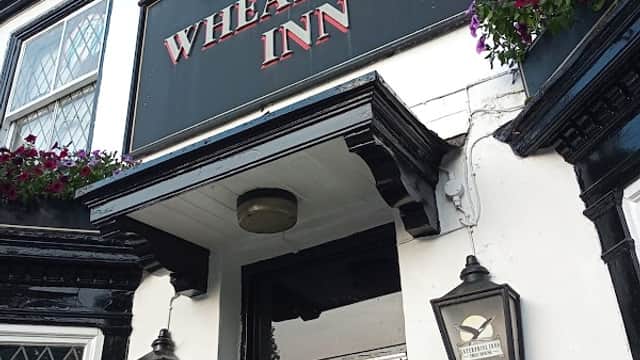 Signage of Wheatsheaf Inn with hanging flower baskets, lanterns, and a menu board outside the entrance.