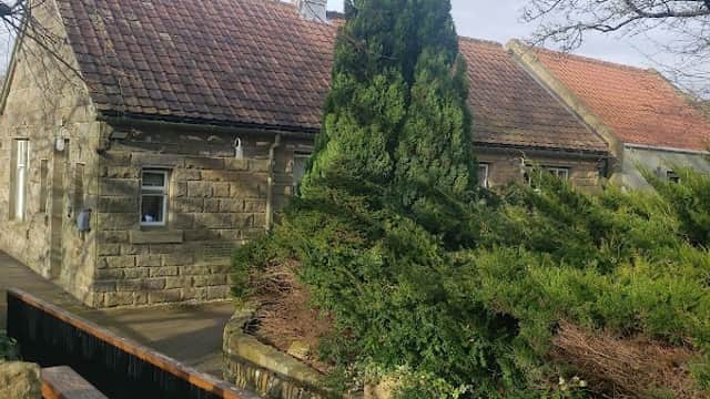The Ley Hall features a stone building with a red-tiled roof, surrounded by lush greenery and trees in Lealholm.