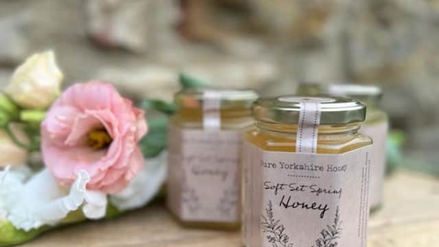 Three jars of Pure Yorkshire Honey on a wooden surface, surrounded by soft pink flowers.