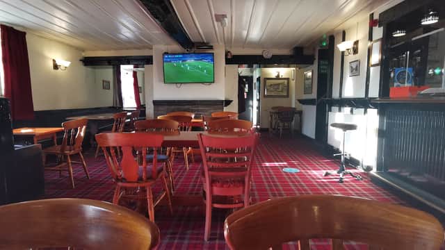Interior of The Toby Jug bar featuring wooden tables, chairs, a bar counter, and a TV showing a sports event.