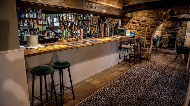 Bar area with wooden counter, stools, stone walls, and shelves lined with various drinks in The Queen's Head, Finghall.