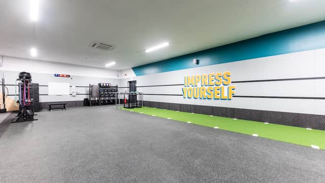 Spacious gym interior with green turf, workout equipment, and a motivational "IMPRESS YOURSELF" wall slogan.
