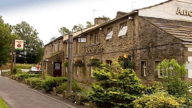Stone building with a sign for Anchor Inn, surrounded by greenery and a pathway in a rural setting.