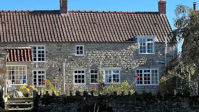 Charming stone farmhouse with a red-tiled roof, surrounded by greenery and a stone wall, under a clear blue sky.
